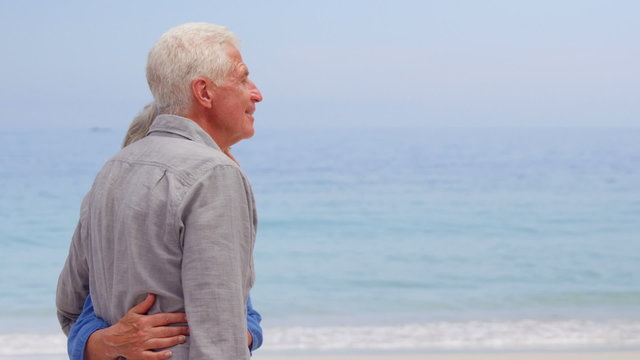 Old couple hugging facing the sea