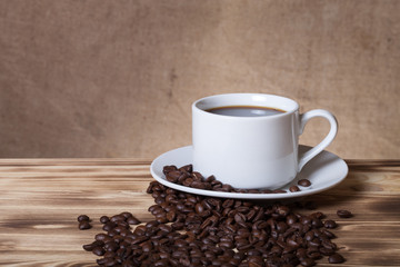 Coffee beans and coffee in white cup on wooden table opposite a