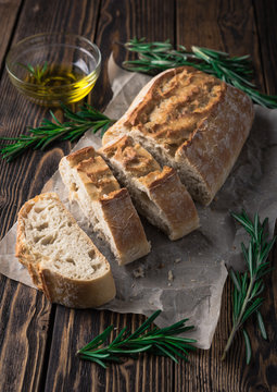Sliced italian bread Ciabatta with rosemary on wooden background