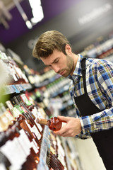 Wine specialist putting bottle up in winery section of supermarket