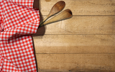 Checkered Tablecloth on Wooden Table / Rustic wooden table partially covered with a red and white checkered tablecloth and two wooden spoons or ladles