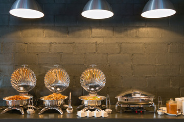 Buffet line food containers shaped shells, with three lighting and dark bricks wall background.
