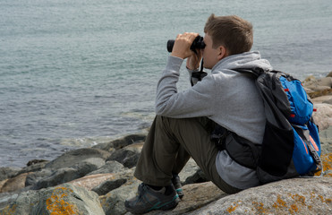 Junge mit Fernglas sitzend an der Küste