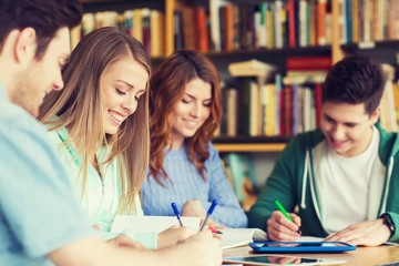happy students writing to notebooks in library