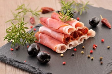 Ham with rosemary and olive on black stone table