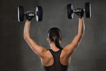 young woman flexing muscles with dumbbells in gym