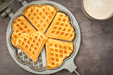 Home made heart shaped waffles served in a traditional cast iron waffle pan with a healthy peanut butter banana smoothie milkshake.