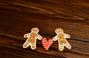 Two handmade cookie in the shape of men and heart in the middle between them on the rough wooden brown background
