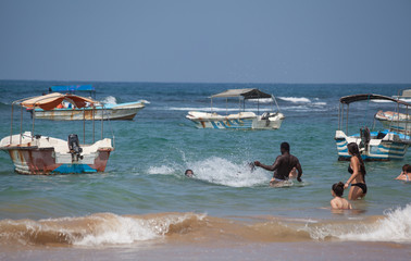 Menschen schwimmen und plantschen zwischen Fischerbooten in den Wellen des türkis-blauen Indischen...