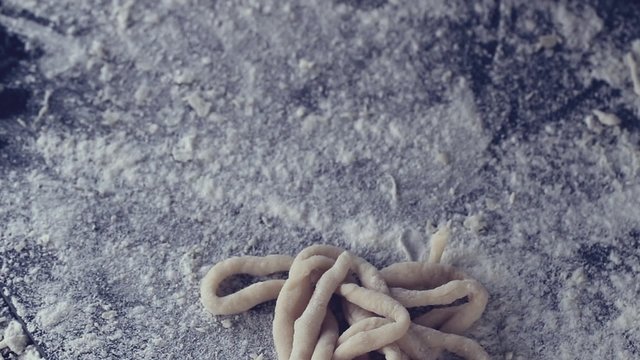 Female hands lay out pasta pici over black table, powdering by flour. Dark rustic style. In retro filter effect