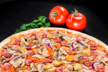 closeup Tasty pizza with mushrooms, ham and pickles on a black b