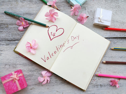 defocused on valentine background concept with heart shape on 14 and pink flowers on white notebook page with gift boxes