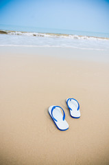 White sandals with blue stripe left on beach.