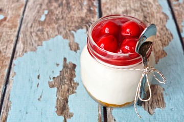Delicious cherry cheesecake in a mason jar with spoon on a rustic wood background