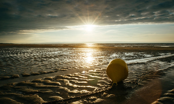 Une bouée en bord de mer à Gabourg par marée basse, en contre-jour au soleil couchant par temps nuageux