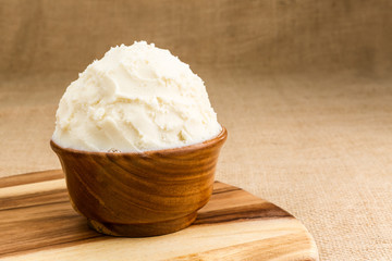 Shea butter in the wooden bowl stands on the wooden board, on th