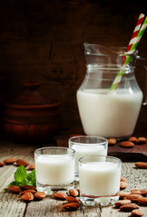 Almond milk in small glasses and spilled dry almonds on old wood