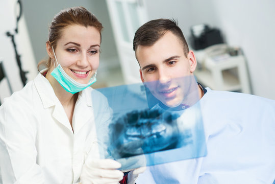 Doctor and patient looking at roentgen of human jaw, focus is on roentgen. Dentist office.