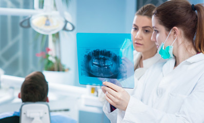 Dentist looking at roentgen of human jaw. Consulting. Patient blurred on chair in background.