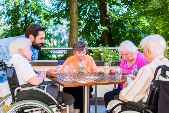 Gruppe Senioren und Pfleger spielen Karten im Seniorenheim