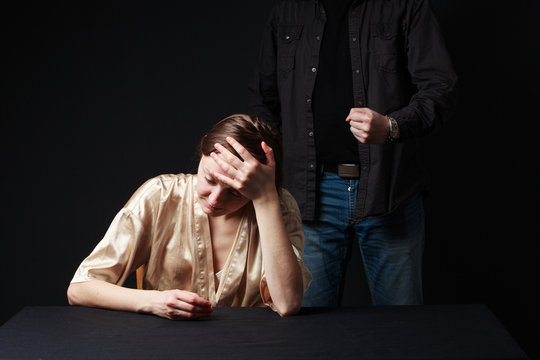Sad woman is sitting , keeping hand on the forehead, man's figur