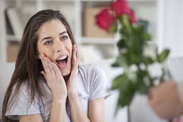 Surprised happy young woman, young man gives her flowers