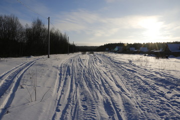 Fototapeta na wymiar Дорога в снегу, идущая вдоль деревни к лесу зимним вечером