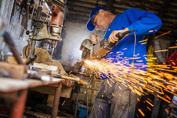 Craftsman sawing metal with disk grinder in workshop.