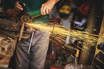 Craftsman sawing metal with disk grinder in workshop.