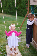 Little girl on a playground riding on a swing in summer