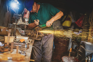 Craftsman sawing metal with disk grinder in workshop.