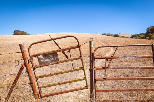 California dry grassland rolling hills landscape with a rusty open gate and sign to close it