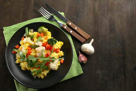 Black plate with vegetable risotto on served wooden table