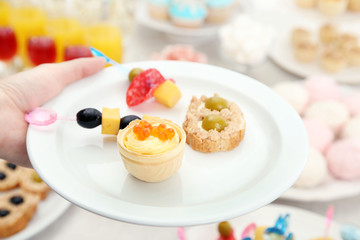 Woman holding plate with snacks and canape on buffet background