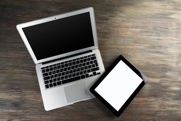 An open silver laptop and modern tablet on the wooden background