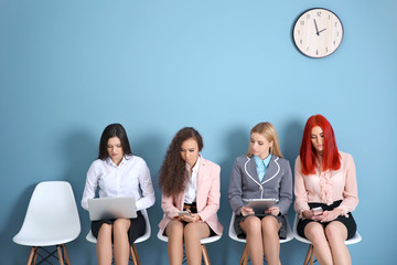 Young businesswomen sitting on a chairs and using devices in blue hall