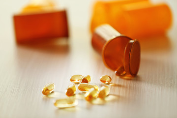 Capsules spilled from orange pill bottle on wooden table, blurred
