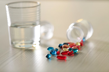 Pile of blue and red capsules with glass of water on the table, close up