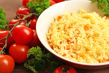 Stewed rice with a carrot on a plate over wooden background, close up