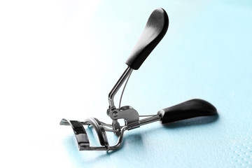 Eyelash curler with black handles on a blue background, close up
