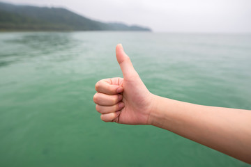 Women hand with thumb up on green sea background,soft focused