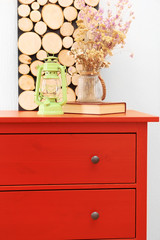 Room interior with red wooden commode, flowers and lantern on light wall background