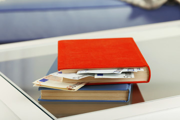 Red and blue books with hidden euro banknotes on glass table