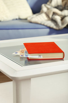 Red book with hidden euro banknotes on glass table
