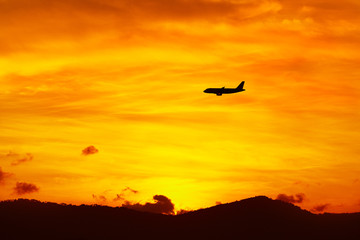 Fototapeta na wymiar Beautiful Landscape. Travel On Summer Vacations To Thailand, Asia. Silhouette Of Flying Aircraft ( Airplane ) In Beautiful Orange Sky, Hills Of Tropical Island During Sunset. Tourism. Transportation.