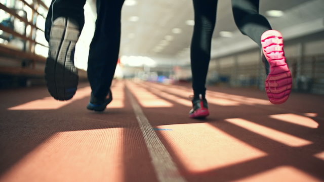 Rear view of male and female feet in athletic shoes running in stadium