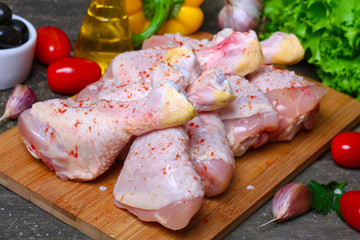 fresh raw chicken legs on a cutting board with vegetables and spices on wooden background