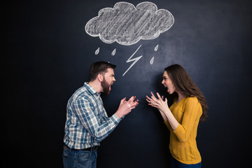 Quarrelling couple standing against background of chalkboard and screaming