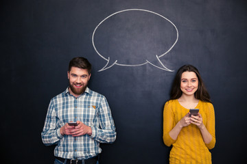 Happy couple using mobile phones over chalkboard with speech bubble