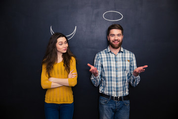 Happy couple playing devil and angel over blackboard background